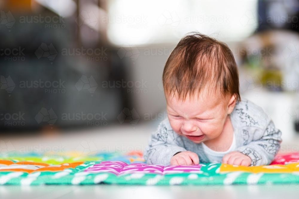 Image of Young baby doing tummy time on a mat on the floor crying