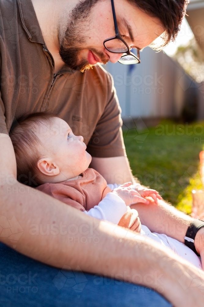 Young baby girl looking up at father in afternoon light - Australian Stock Image