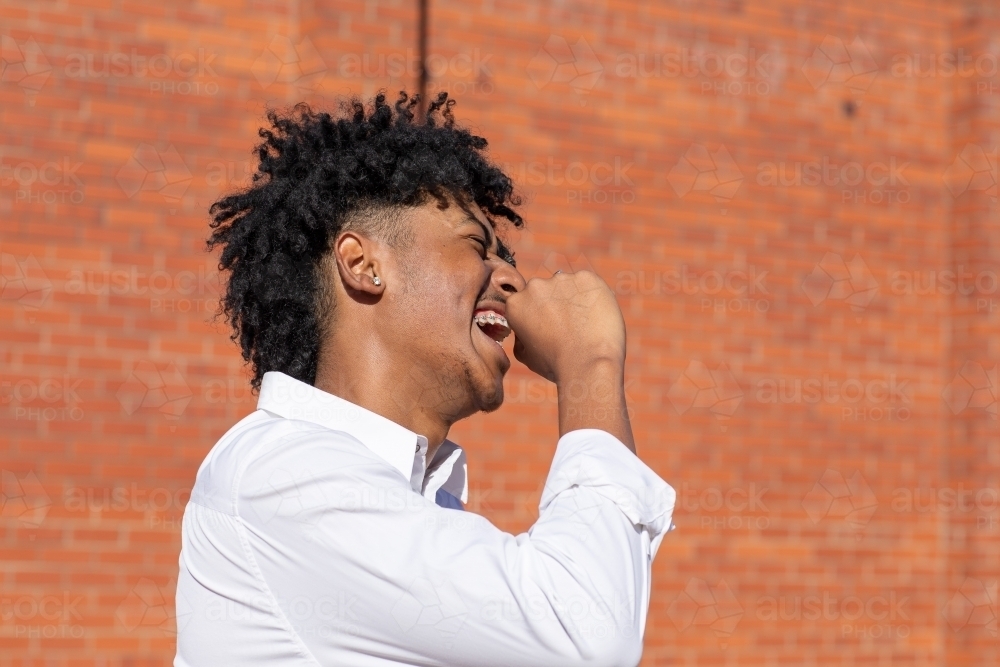 young bloke laughing in profile in front of brick wall - Australian Stock Image