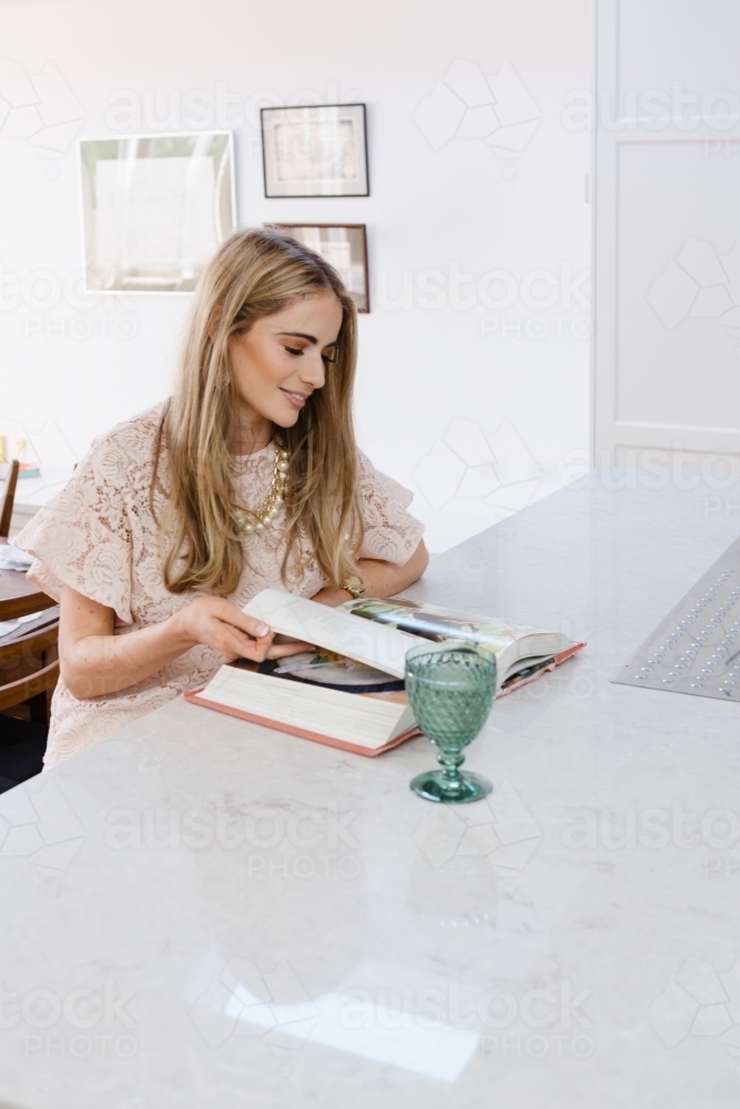 Young blonde woman reading a cookbook at the kitchen counter - Australian Stock Image