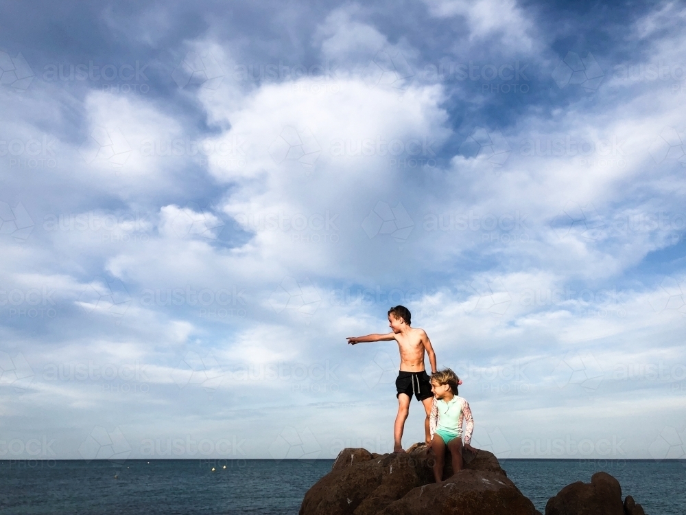 Young Boy and girl standing on top of coastal rocks pointing out to sea - Australian Stock Image