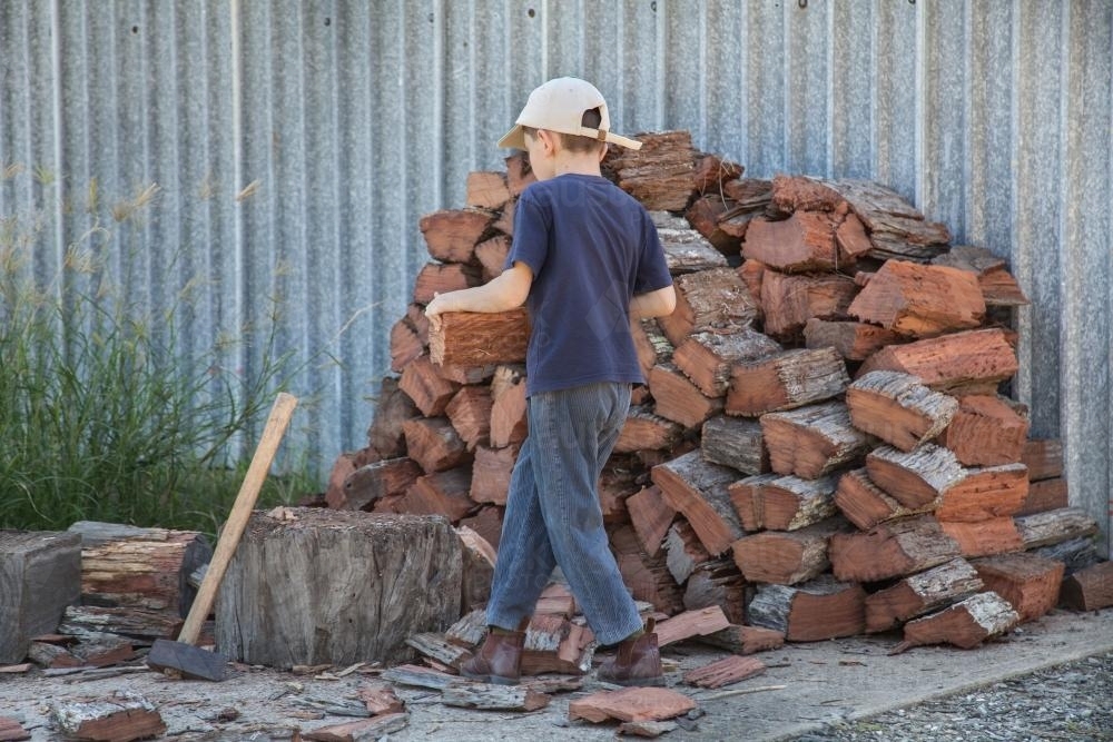 Young boy carrying wood to chop - Australian Stock Image