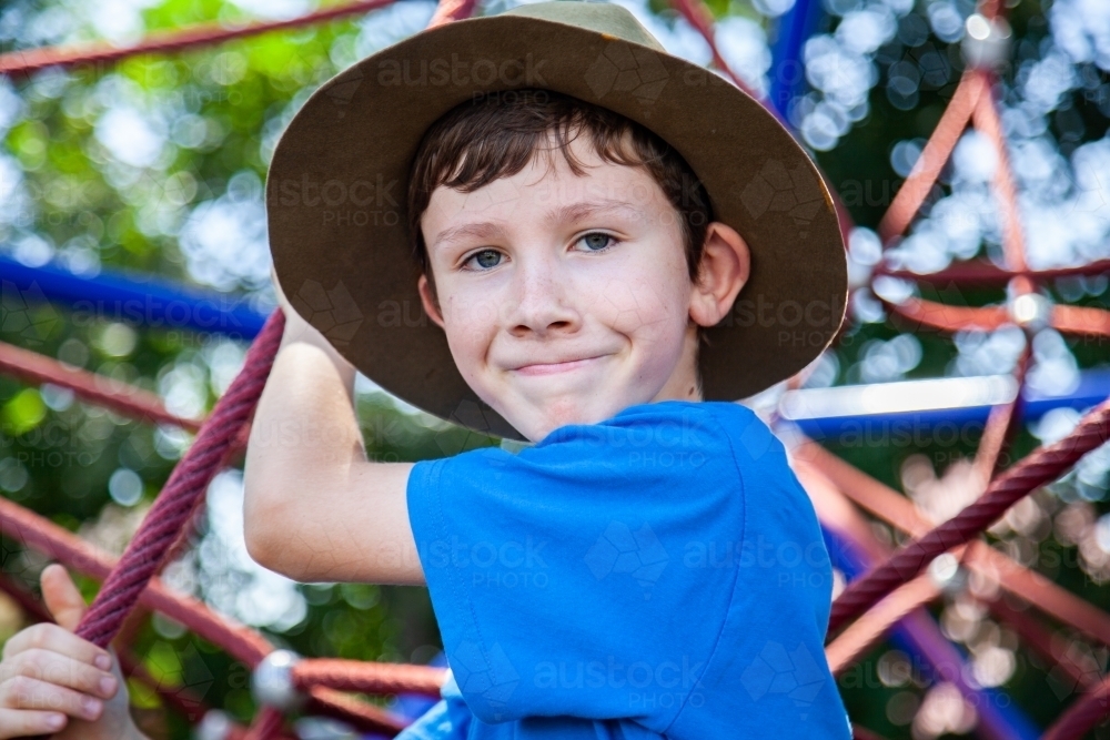 Young boy climbing spiderweb playground equipment at park - Australian Stock Image