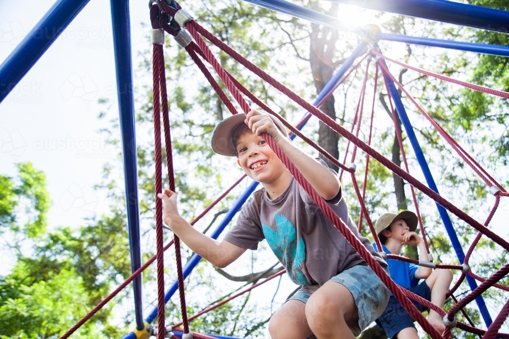 Young boy climbing spiderweb playground equipment at park - Australian Stock Image