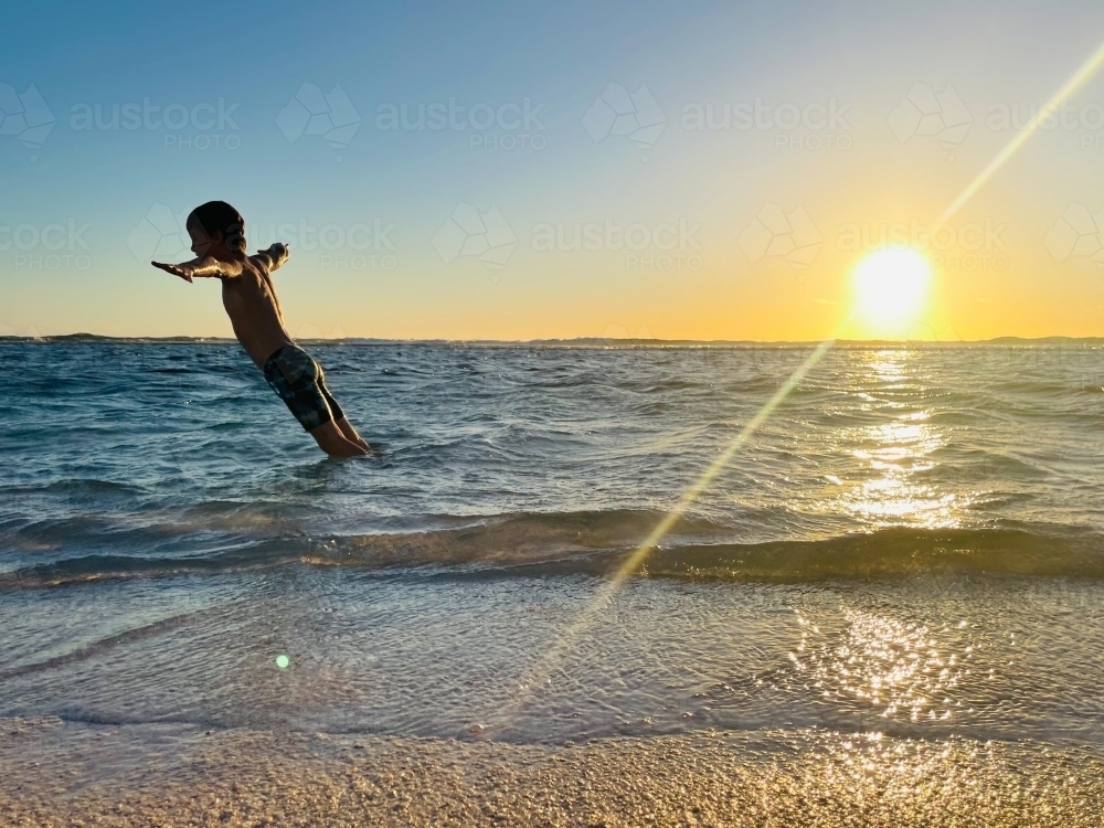 Young boy falling into ocean with sun setting in background - Australian Stock Image