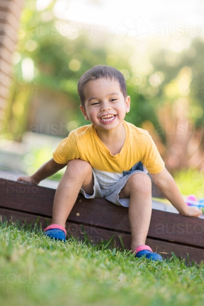 Young boy happily sitting on deck next to his eggs after easter egg hunt. - Australian Stock Image