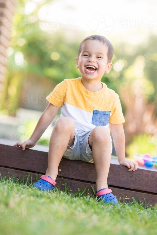 Young boy happily sitting on deck next to his eggs after easter egg hunt. - Australian Stock Image