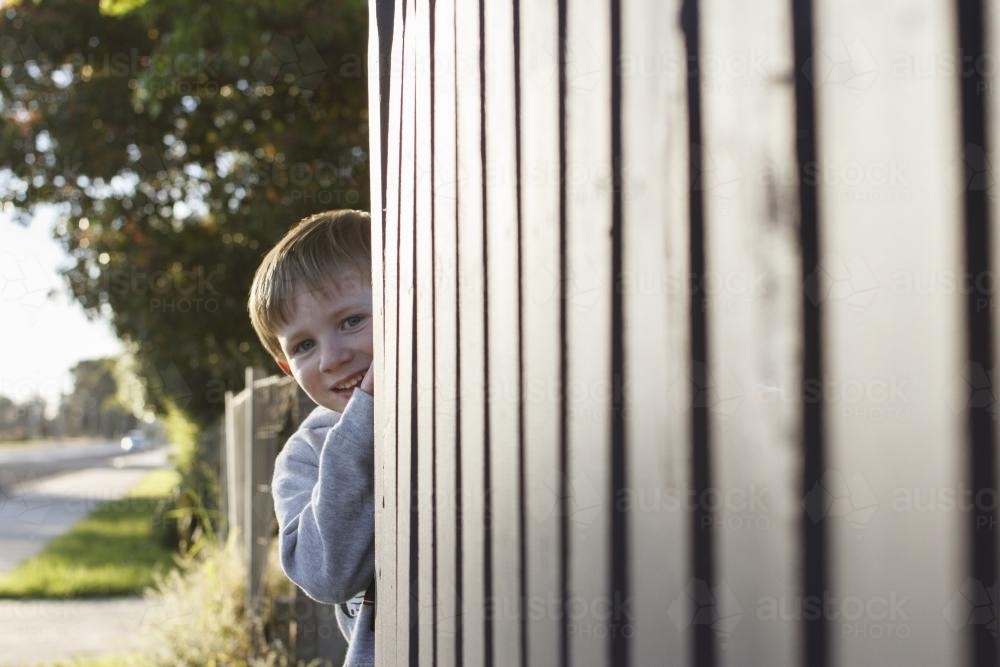 Young boy hiding behind fence - Australian Stock Image