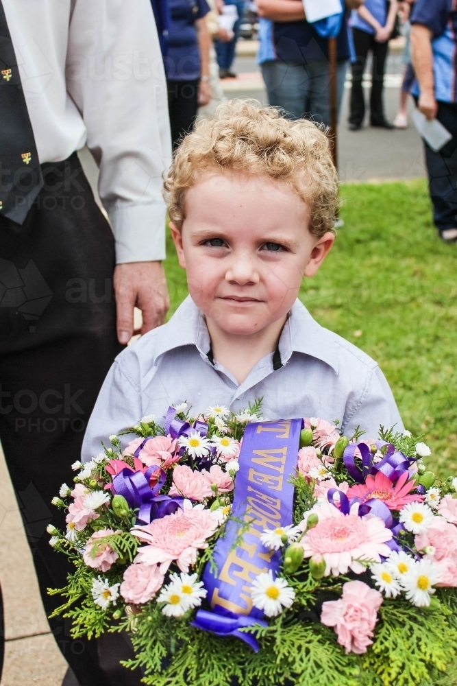 Young boy holding flower wreath with lest we forget sash for Anzac Day - Australian Stock Image