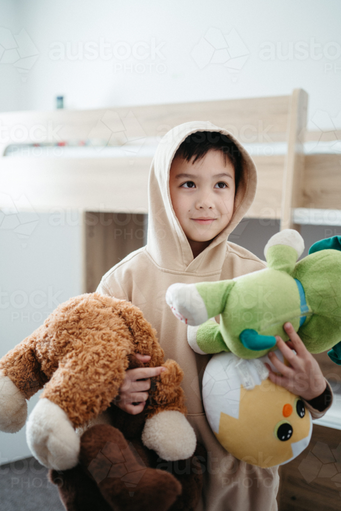 Young boy holding plush toys inside his bedroom - Australian Stock Image