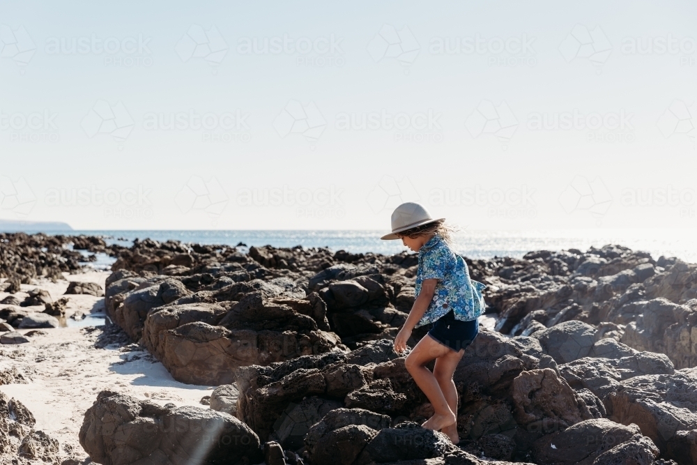 Young boy in hat walking amongst rock pools - Australian Stock Image