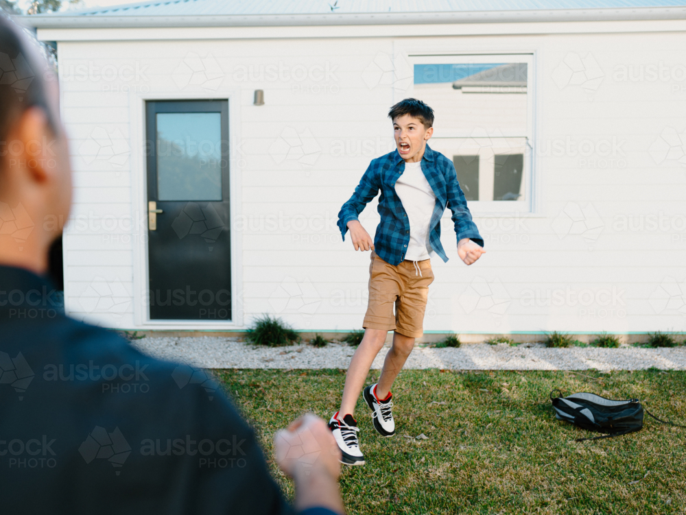 Young boy jumping in their yard playing game with dad - Australian Stock Image