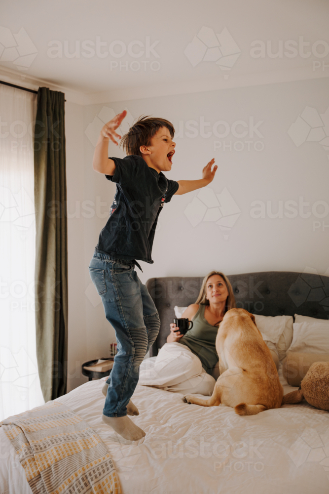 Young boy jumping on the bed happily. - Australian Stock Image