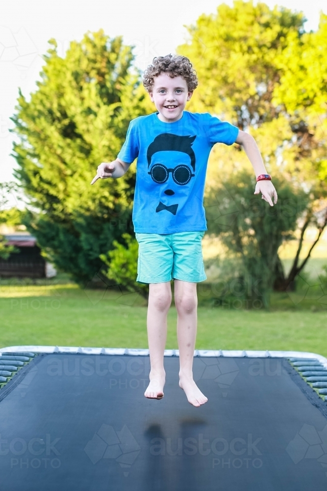 Young boy jumping on trampoline smiling - Australian Stock Image