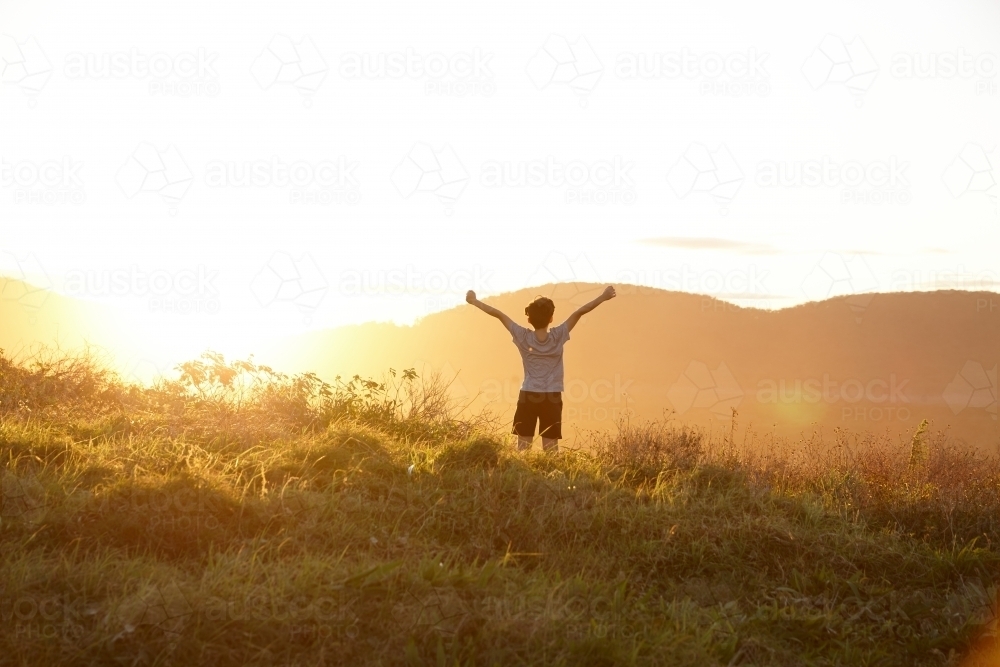 Young boy looking out to mountains at sunset - Australian Stock Image