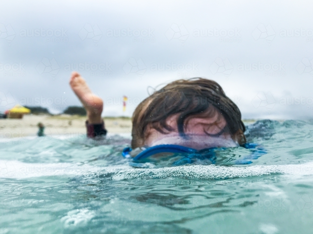 Young boy looking through mask underwater with moody sky - Australian Stock Image