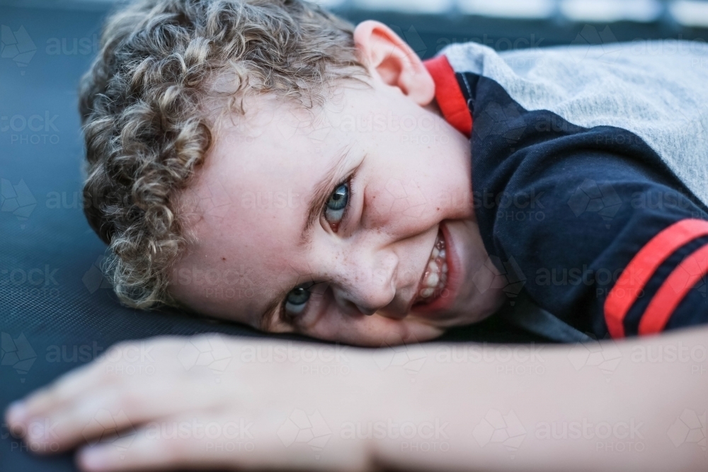 Young boy lying down on trampoline happy laughing - Australian Stock Image