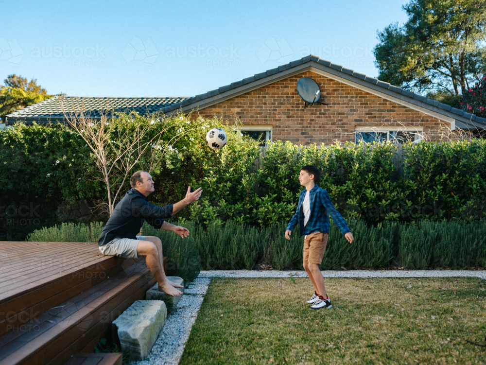 Young boy playing soccer on their garden deck with his father. - Australian Stock Image