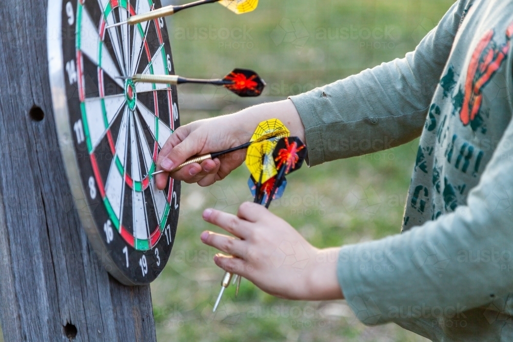 Young boy pulling throwing darts of game board - Australian Stock Image