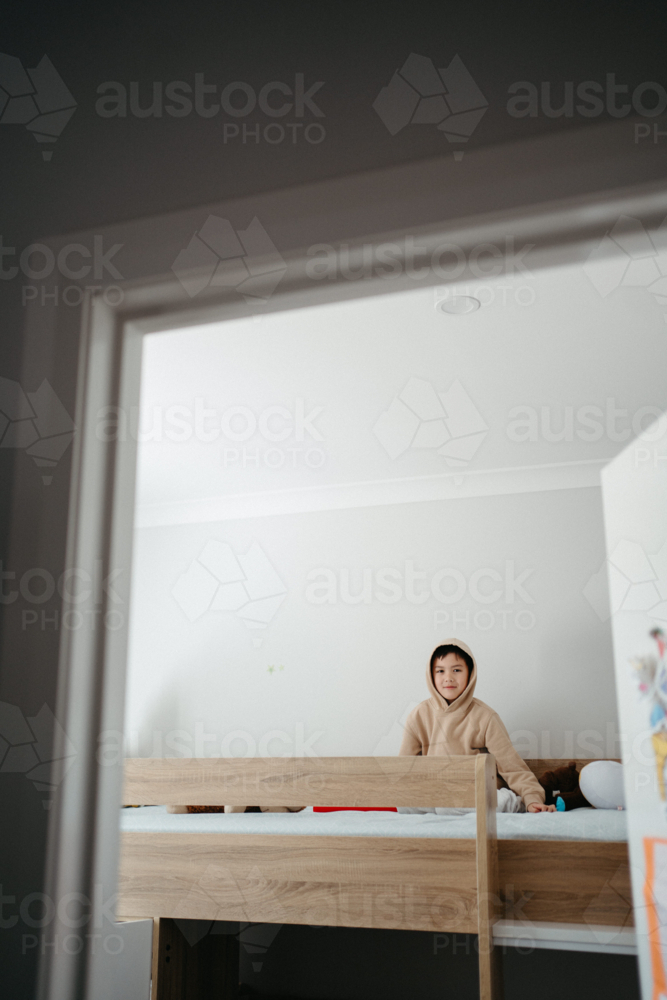 Young boy sitting on top of the bunk bed. - Australian Stock Image