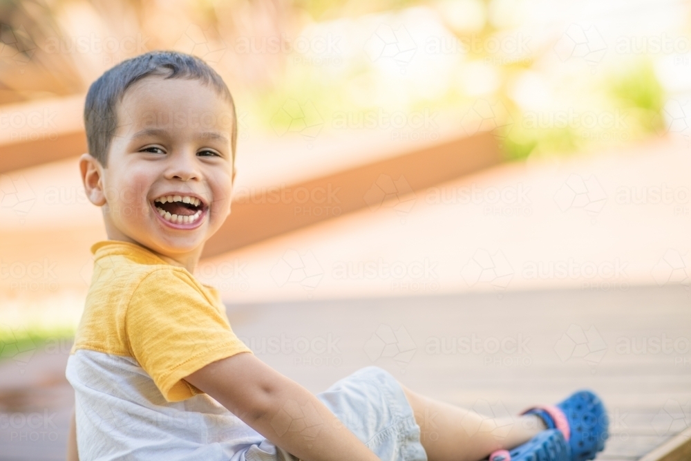 Young boy sitting outside, smiling at the camera - Australian Stock Image