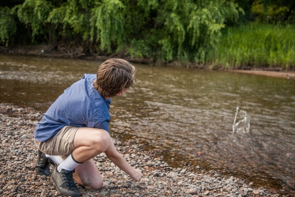 Young boy skimming stones beside a river - Australian Stock Image