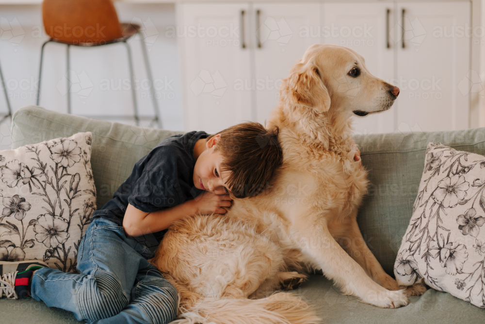 Young boy snuggles with his pet dog on the couch. - Australian Stock Image