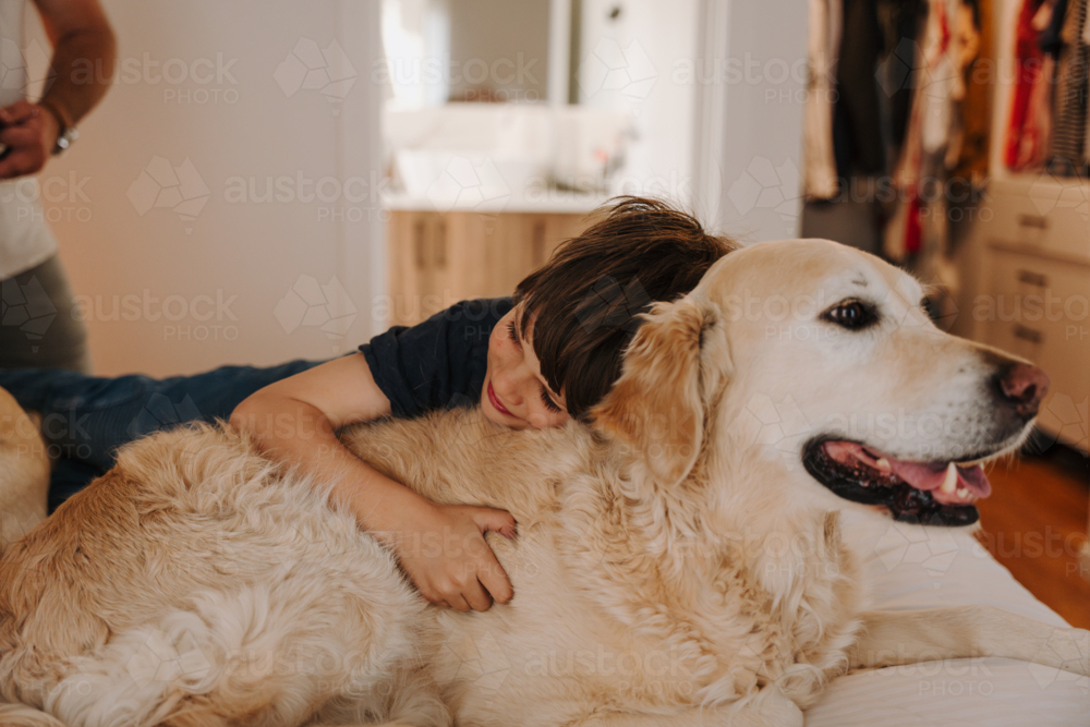 Young boy snuggling with a golden retriever dog. - Australian Stock Image