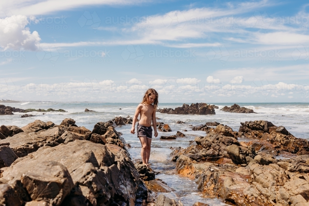 Young boy standing in ocean between rocks - Australian Stock Image