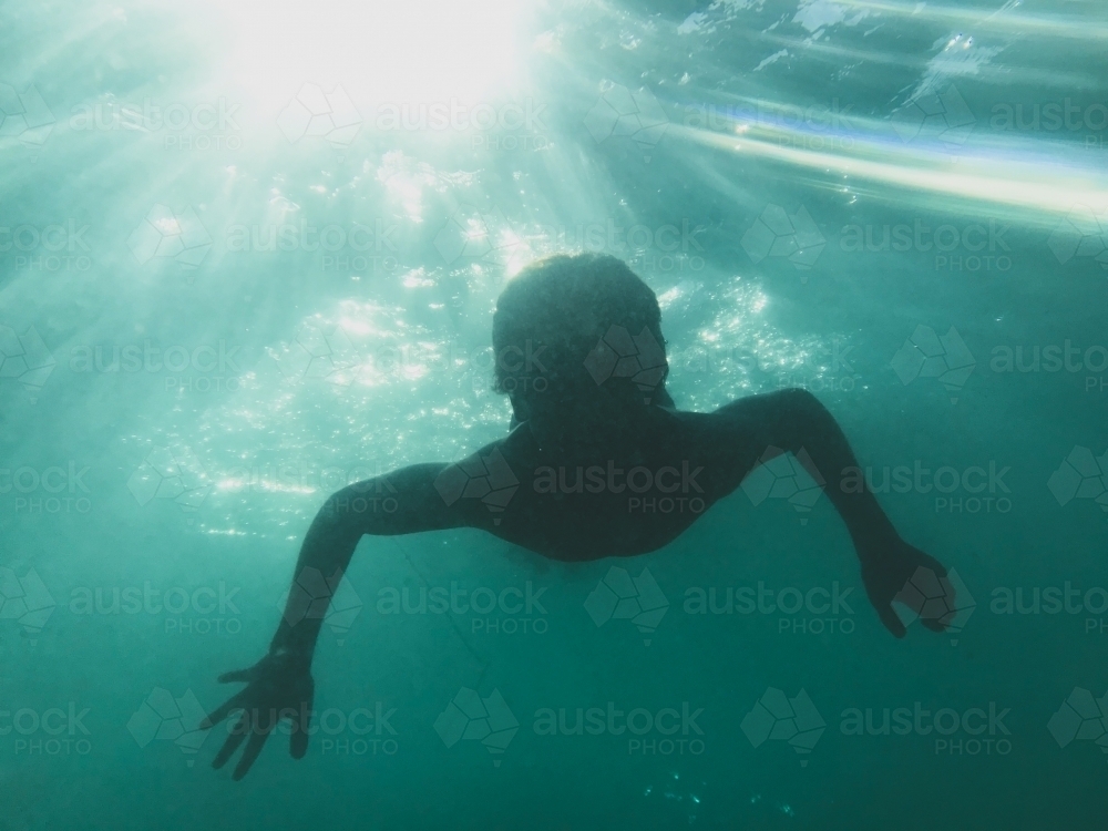 Young boy swimming underwater with sun beams through water - Australian Stock Image