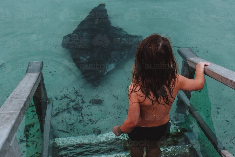 Young boy walking down ocean stairs towards stingray - Australian Stock Image