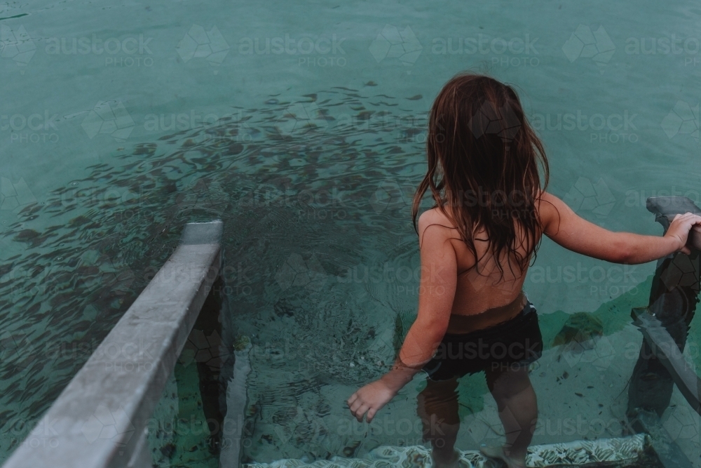 Young boy walking into water with school of fish - Australian Stock Image