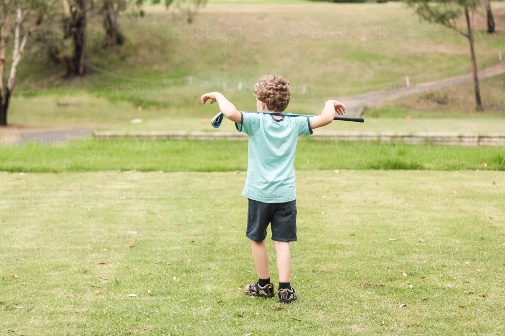 Young boy walking on golf green with golf club over shoulders - Australian Stock Image