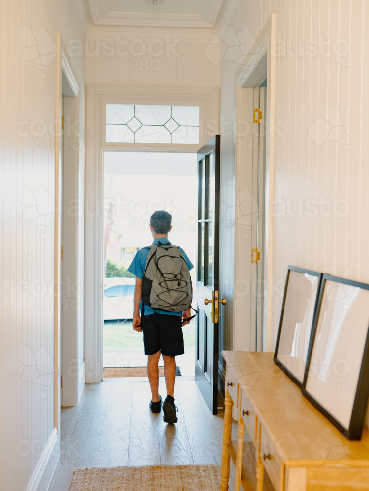 Young boy walking towards the door along the hallway. - Australian Stock Image