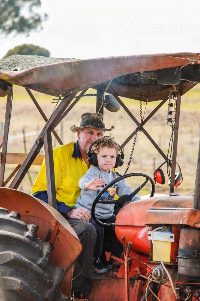 Young boy waving sitting on farmer's lap on tractor - Australian Stock Image