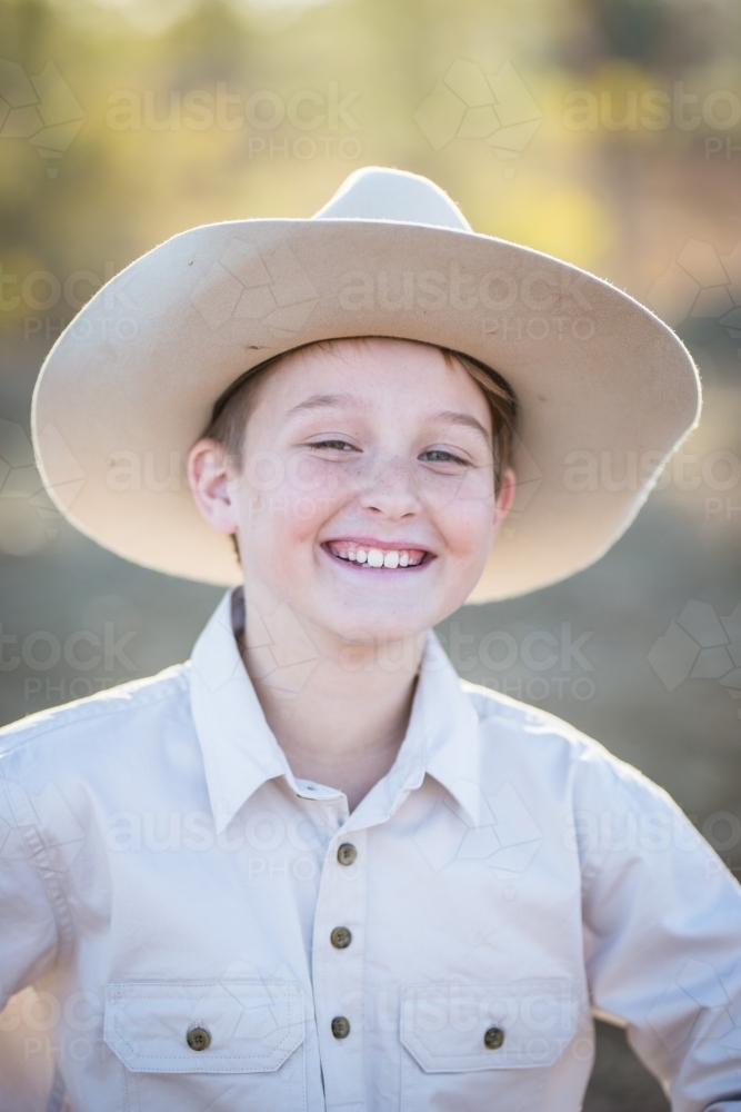 Young boy wearing akubra hat laughing on family farm in drought - Australian Stock Image