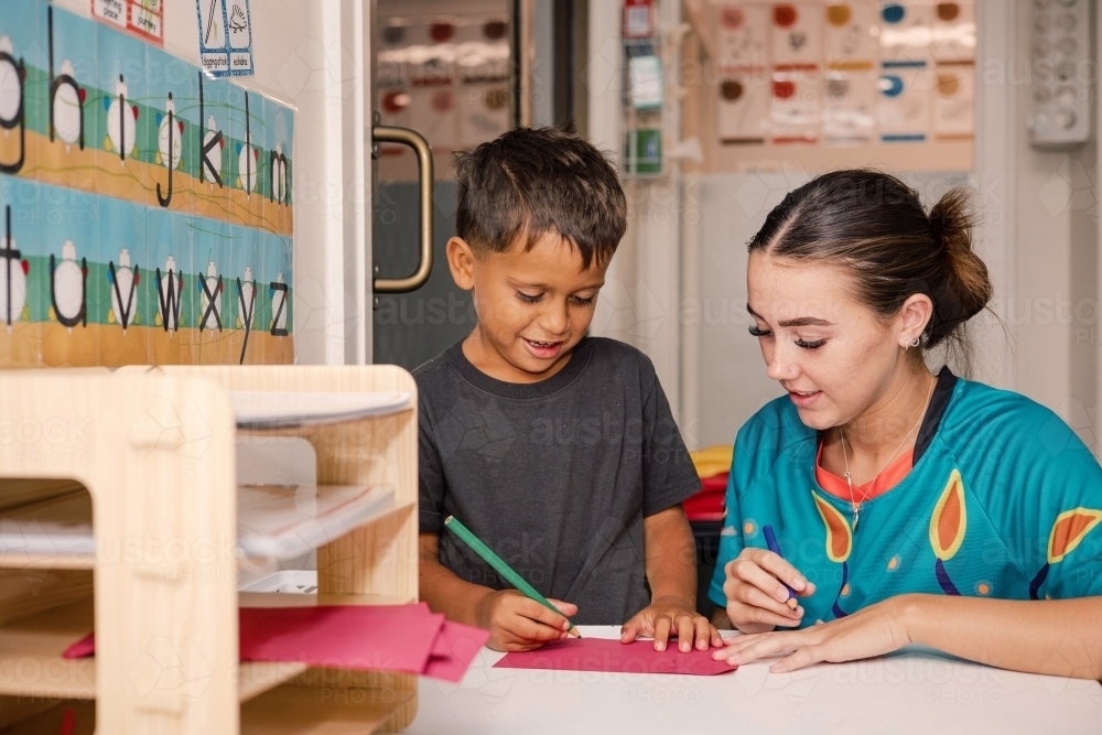 Young boy writing with educator - Australian Stock Image