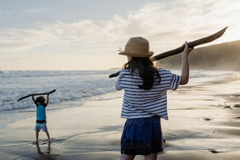 Young brother & sister (young boy and girl) holding sticks like spears playing together at the beach - Australian Stock Image