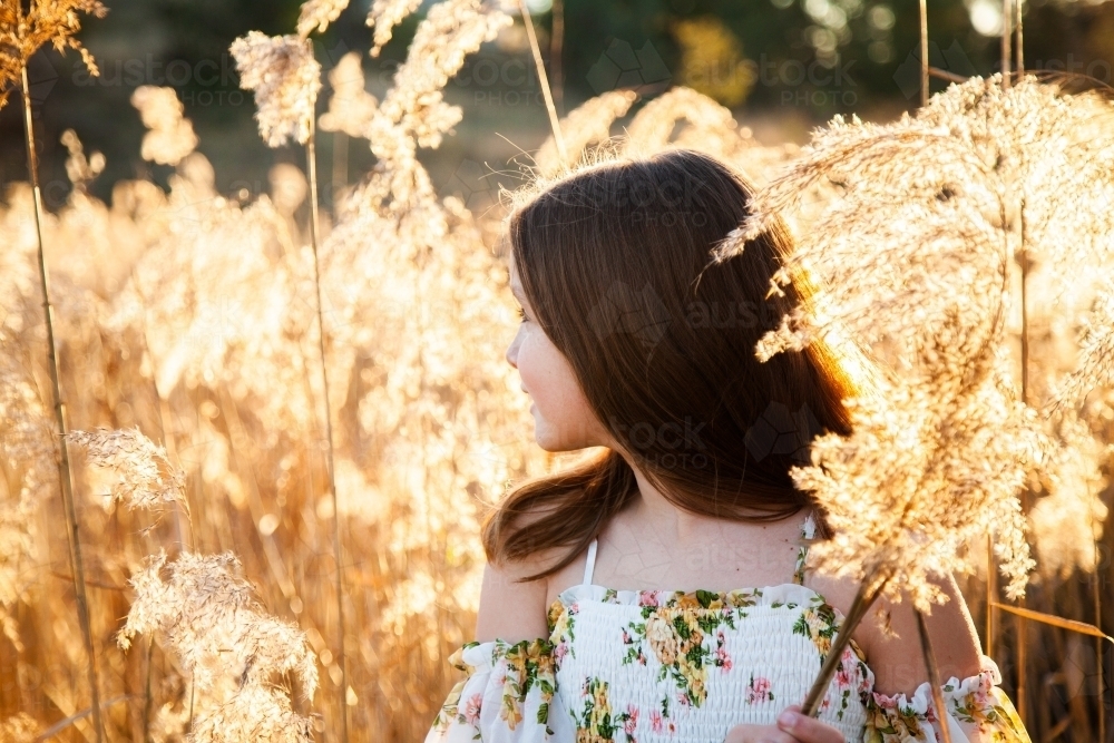 Young brunette girl looking off into the distance backlit by golden light - Australian Stock Image