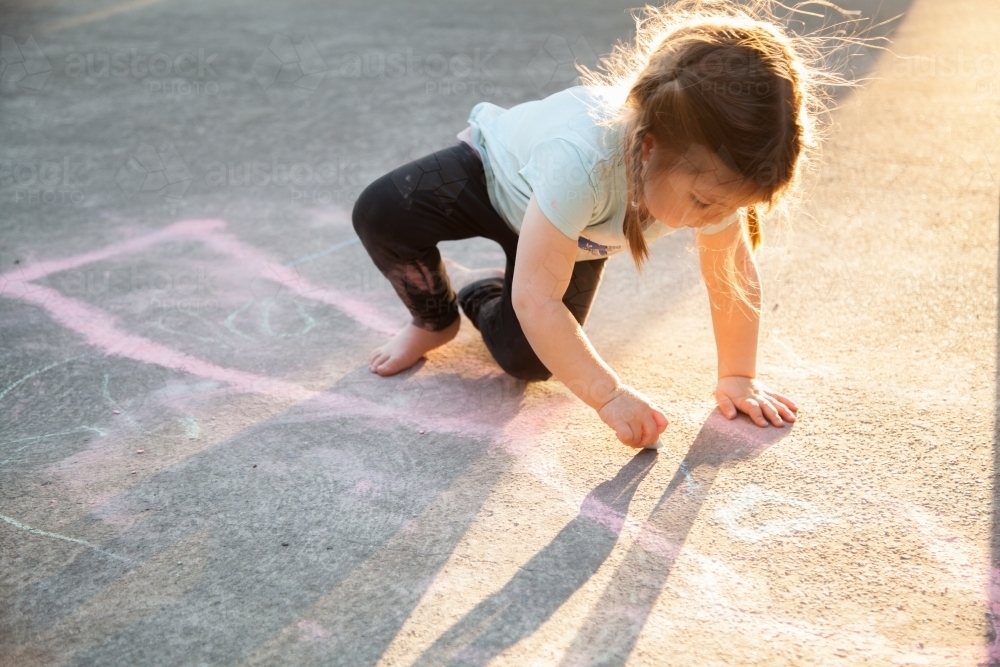 Young child drawing on concrete with coloured chalk in the afternoon - Australian Stock Image