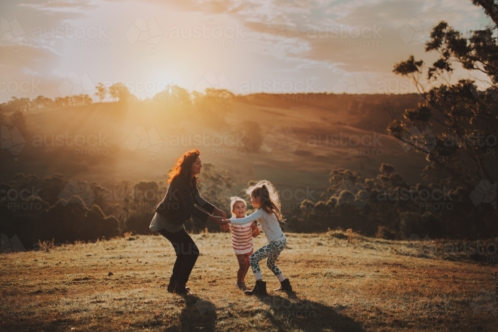 Young children playing with their mother in a field at sunset - Australian Stock Image