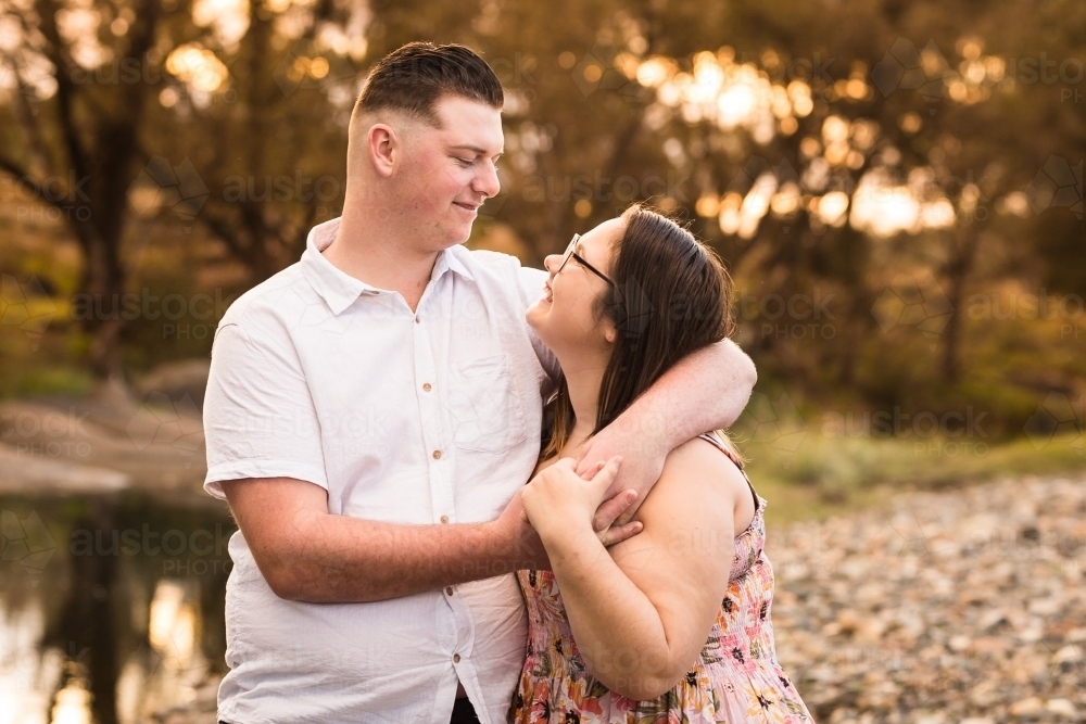 Young couple man with arms around girlfriend looking at each other smiling - Australian Stock Image