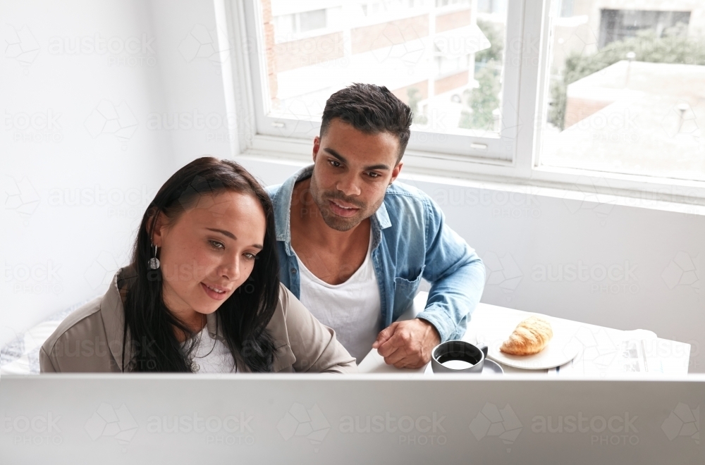 Young couple shopping online over breakfast - Australian Stock Image