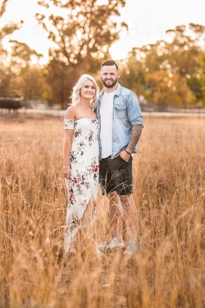 Young couple standing arm in arm in paddock smiling - Australian Stock Image