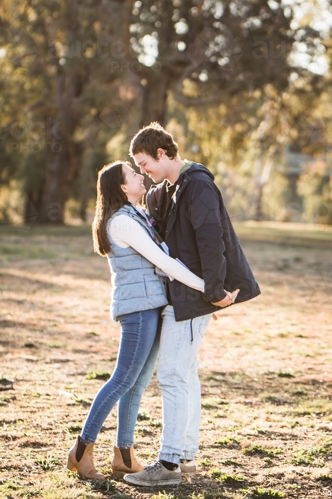 Young couple standing close together holding hands looking at each other smiling - Australian Stock Image