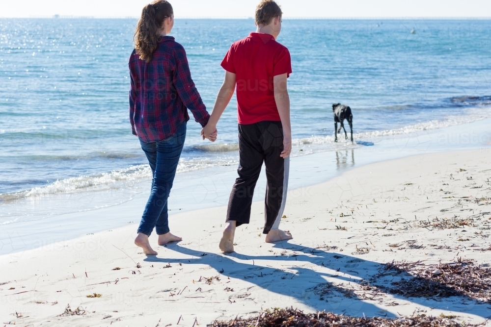 Young couple walking along beach holding hands - Australian Stock Image