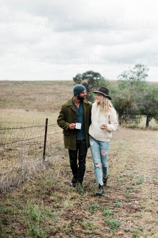 Young couple walking through farm holding cups of coffee - Australian Stock Image