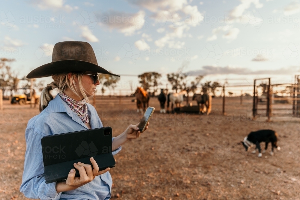 Young cowgirl using her phone and tablet at the farm - Australian Stock Image