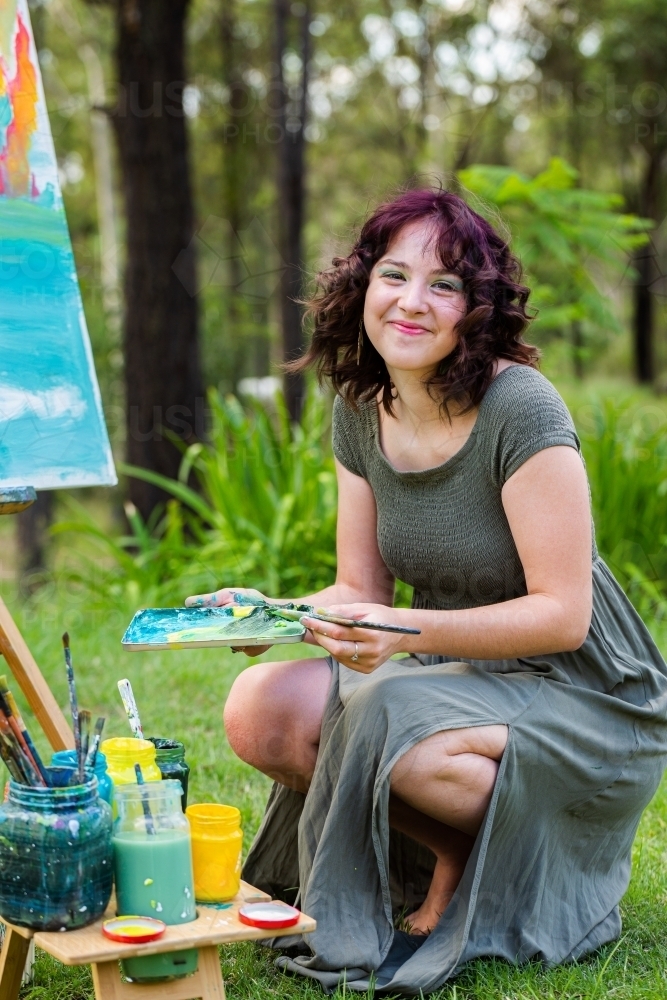 Young creative artist with curly purple hair mixing paints for art - Australian Stock Image