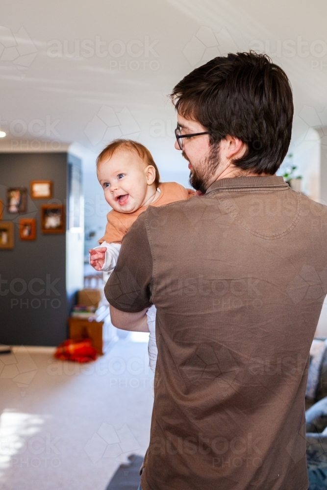 Young dad cuddling his smiling four month old baby inside home - Australian Stock Image